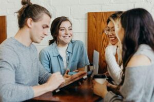 Four friends sit around a table chatting happily for ‘Exclusive Alternative Asset Deals: Grow Your Wealth and Help Others!’